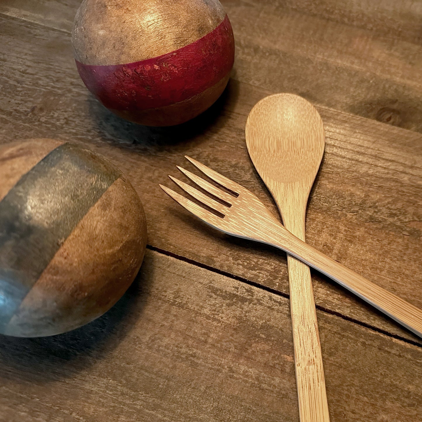 A bamboo fork and spoon from a Sarita set rest next to vintage wooden croquet balls on a table.