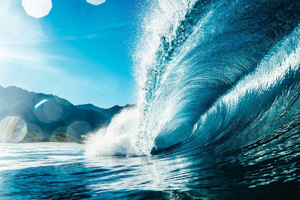 A beautiful blue photo of a crashing wave as water droplets reflect the sunlight.