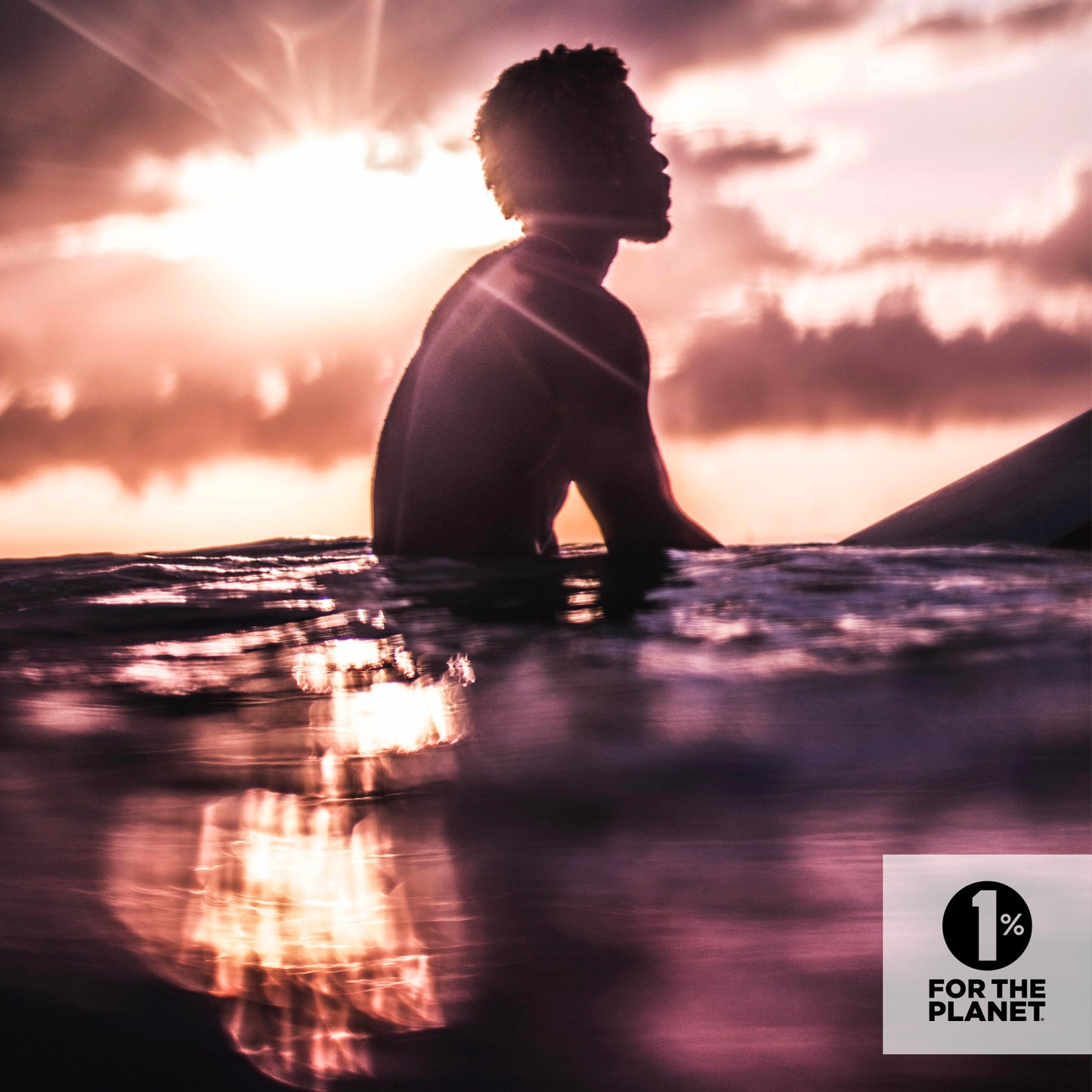 Photo of a man sitting atop a surfboard & looking out over the ocean at dusk