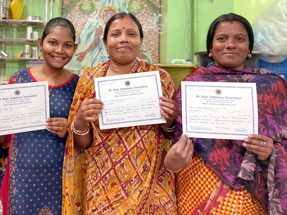 Three Indian women stand, smiling, as they proudly hold up certificates for the camera. They are dressed in traditional (and colorful) sari dresses.