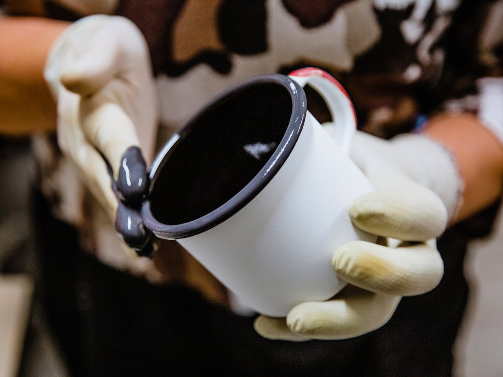 A craftsman applies pigment to an enamelware mug during production