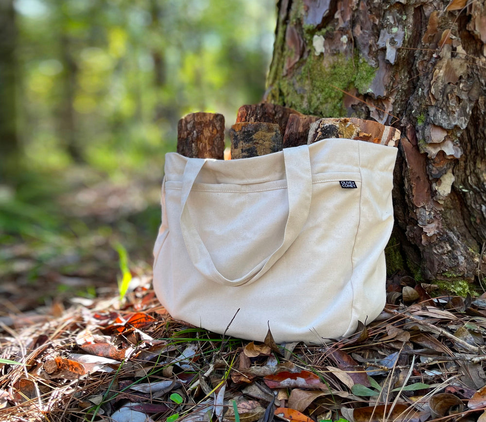A Sonoma bag filled with firewood sits propped against a mossy tree in a forest