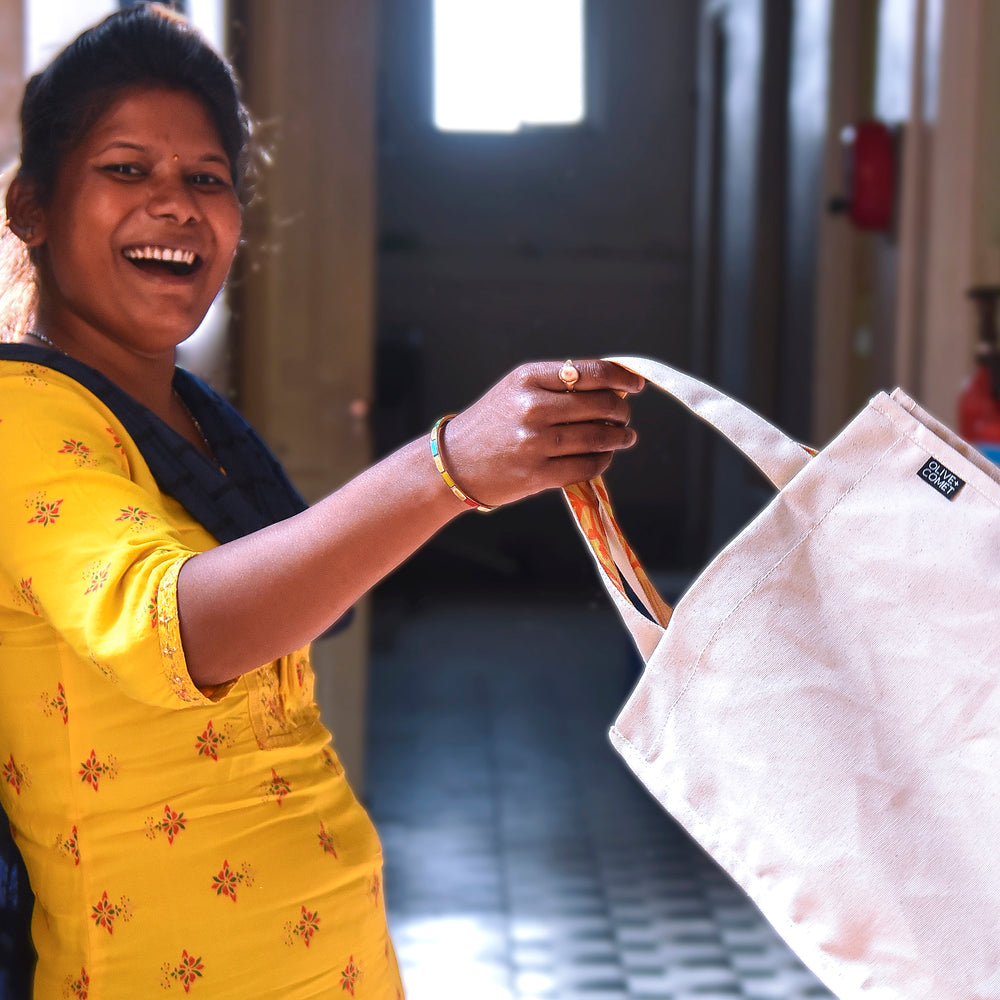 A woman at our fair trade production facility smiles while swinging a recently finished Parker bag in her hand