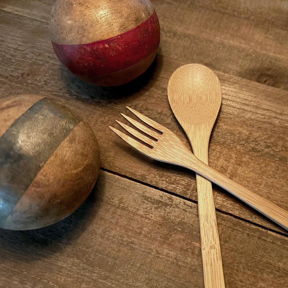 
                  
                    A bamboo fork and spoon from a Sarita set rest next to vintage wooden croquet balls on a table.
                  
                
